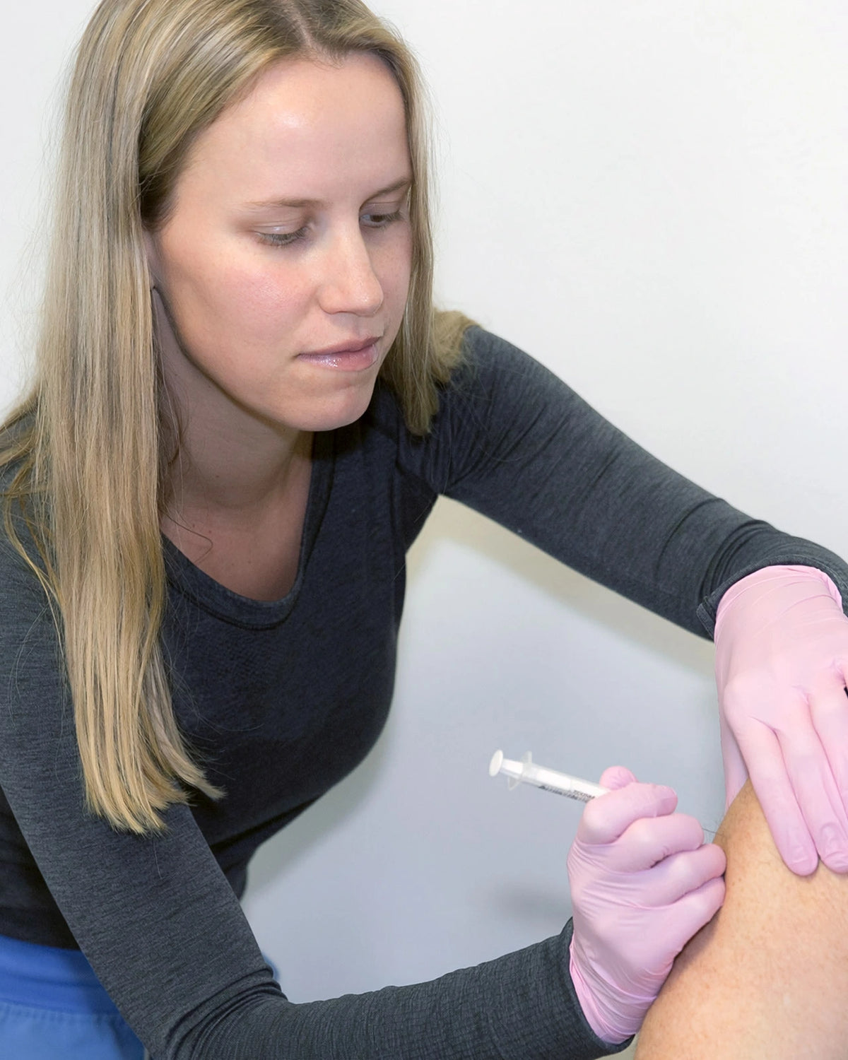 A provider in purple scrubs administering a peptide injection to a patient on an exam table